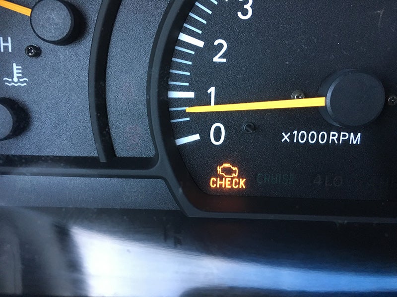 Close-up of a vehicle dashboard tachometer displaying an illuminated check engine warning light.
